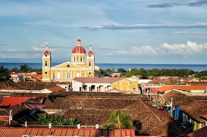 Die gelbe Kathedrale von Granada über roten Ziegeldächern, dahinter der Nicaraguasee